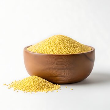 A wooden bowl filled with millet grains sits on a white surface with some spilled beside it.
