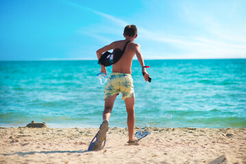 Boy running into the sea with swimming mask and fins on a sunny beach, summer vacation and active lifestyle concept © ольга дубровная
