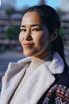 Candid outdoor shot of a smiling woman in a knit jacket and fleece coat, soft daylight, urban backdrop, casual style, confident expression, seasonal fashion, warm approachable mood, modern vibe