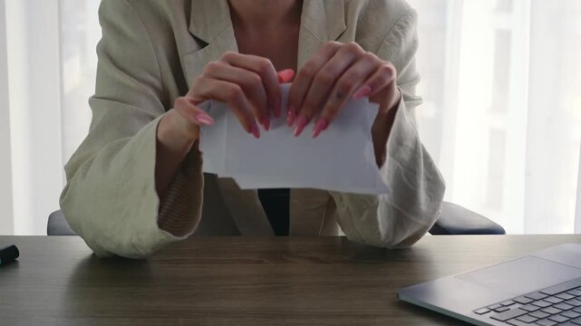 A businesswoman demonstratively tears up a paper document while sitting at her desk in an office.
A businesswoman destroys a document by tearing it into tiny pieces.
Document, paper, form, tear, offic