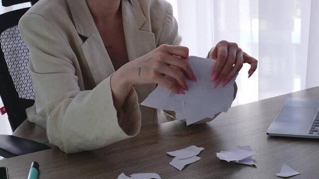 A woman at her desk in an office tears paper into tiny pieces in anger.
Anger at work.
A ruined sheet of paper containing information.
Paper trash in a businesswoman's hand.