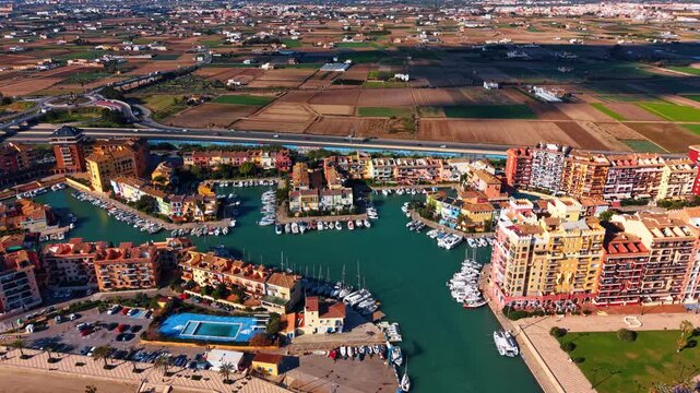 Aerial view of Port Saplaya harbor and agricultural fields. Drone shot of colorful residential buildings around a marina with boats near Alboraya fields.