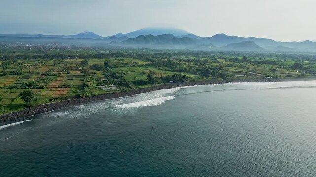 Wide aerial bay panorama with calm surf, green hinterland and distant volcanic silhouettes sweeping drone footage for tourism campaigns, coastal conservation visuals and serene,Bali island,Indonesia