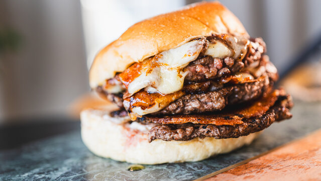 Massive triple smash burger stacked with crispy seared beef patties, melted fried cheese, homemade creamy sauce and soft toasted bun, served on a rustic wooden board with cinematic lighting and green 