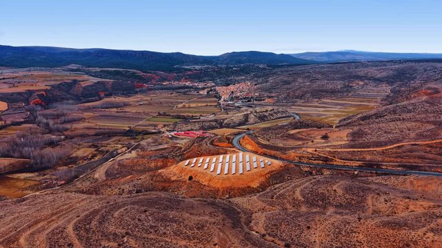 Solar panel array on hill overlooking small Spanish village. Photovoltaic panels installed on a leveled hilltop with a valley and small town in the background, Teruel.