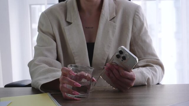 Time out at work.
A woman drinks water and spends time on social media.
A businesswoman holds a touchscreen mobile phone.
Water, office, work, glass, mobile phone