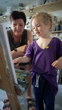 Child painting with an grandmother in a cozy art studio. Candid indoor moment of creativity and learning. Artistic lifestyle scene with real people and natural light.