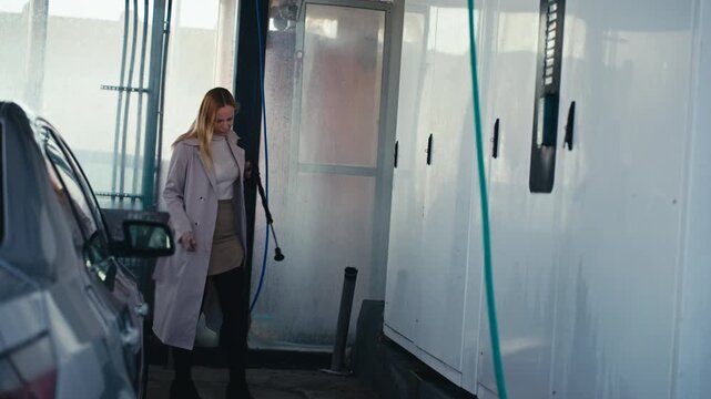 Confident business woman struggling with tangled hose and payment at a self-service car at self service car wash.  Concept of independence, modern lifestyle and breaking stereotypes