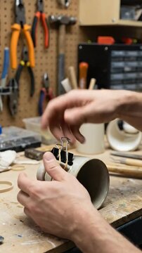 Hands carefully assemble small parts on a workbench in a workshop filled with tools.