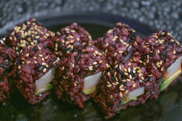 Fototapeta premium black rice sushi rolls background purple dark grains surface close up japanese uramaki with sesame seeds avocado and crab sticks concept of gastronomy, restaurant, healthy eating