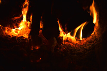 Fototapeta premium firewood burns, fire coals at night. Red hot coals glowing. Orange glow from the coals at the stake at night. flames on a black background. Close-up of flame in fireplace, warmth and comfort