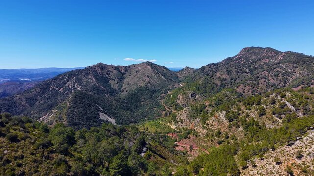 Panoramic view of Sierra de Espadan nature park in Valencia, Spain, showing forested mountain ridges, winding paths, and clear blue sky on a sunny day