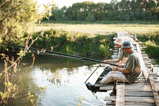 Two fishermen with fishing rods on a footbridge near the lake at summer