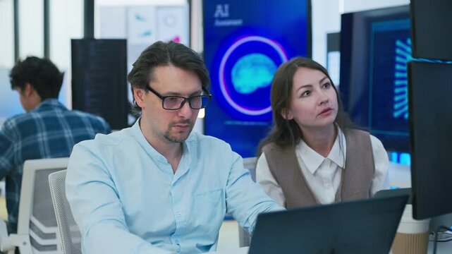collaborative AI development team in modern tech office: young male developer coding on laptop, female team leader in light blue blazer pointing at code and neural network visualization	