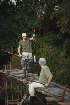 Two fishermen with fishing rods on a footbridge near the lake at summer