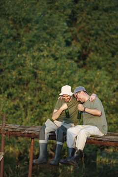 Two fishermen with fishing rods on a footbridge drinking a beer