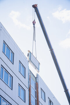 Mobile crane installing wall panel above residential building facade, reflecting prefabricated assembly methods and construction workflow