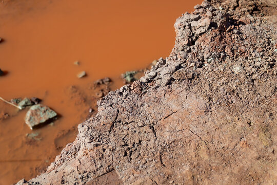 Rocky excavation slope above standing brown water, reflecting drainage problems, unstable ground, and construction site challenges