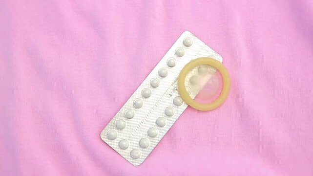 Contraceptive pill packet with condom on pink background.