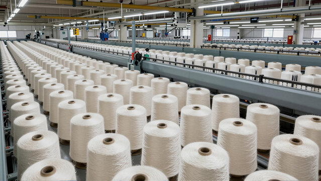 Rows of white yarn spools line up on modern textile manufacturing machinery. This industrial factory showcases automated production processes, essential for the global textile industry