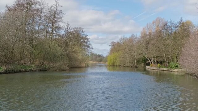 the River Bure in the Norfolk Broads, filmed from Belaugh Staithe. Trees line the riverbank capturing the quiet charm of a perfect summer day on the Norfolk Broads. Panning shot

