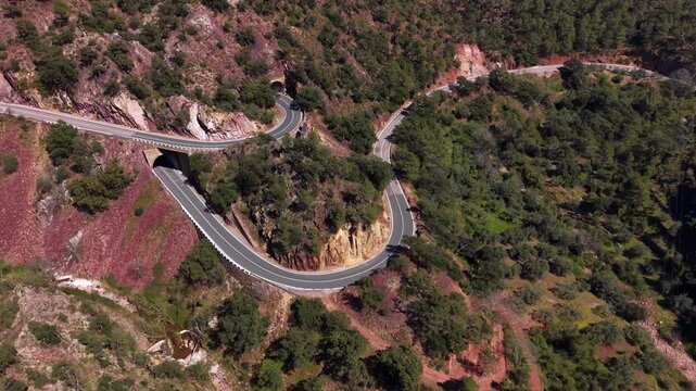 Winding hairpin road with sharp curves carved into the rocky forested slopes of Sierra de Espadan natural park in Valencia, Spain, surrounded by pine trees and red rock formations