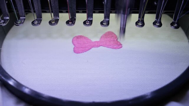 Embroidering an ribbon with an industrial embroidery machine on textile with pink thread.