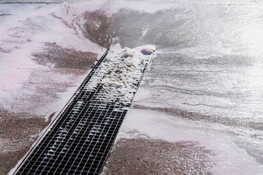 Foamy wastewater flowing into linear trench drain on wet concrete surface, illustrating industrial cleaning runoff management, sanitation systems and facility maintenance