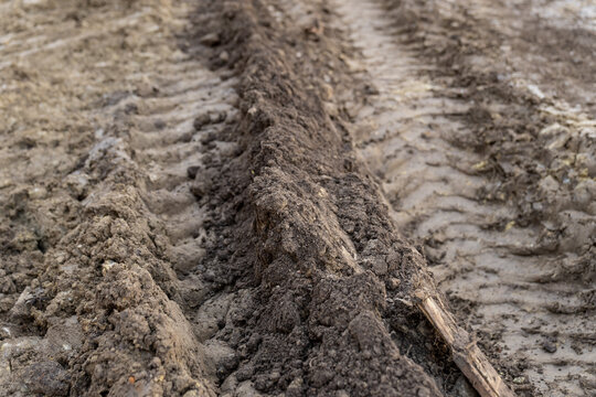 Heavy equipment tire and track impressions carved into wet earth, highlighting construction logistics, terrain damage and site preparation work