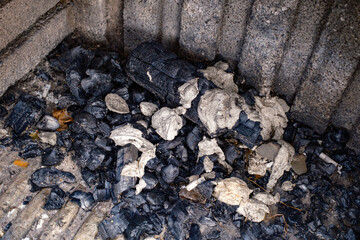 Fototapeta premium Close angle looking into a sturdy stone outdoor barbecue pit filled with cold black charcoal chunks and fine white powdery ash displaying interesting textures and contrasts