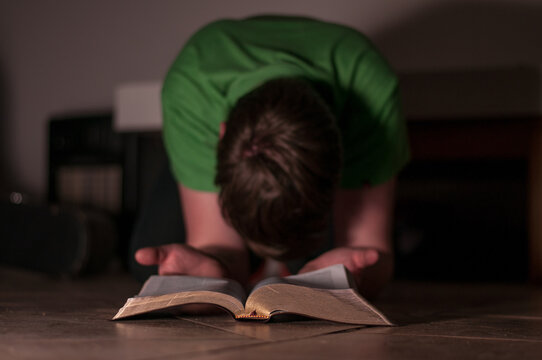 A young man bows down and prays with Bible in hand