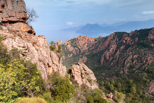 Aerial coastal view of Calanques de Piana, Corsica with red rocks and blue sea under cloudy sky
