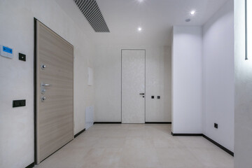 Obraz premium A room is seen with a closed door, plain walls and a clean floor. There is a wall switch and ventilation. Natural light enters through a small source