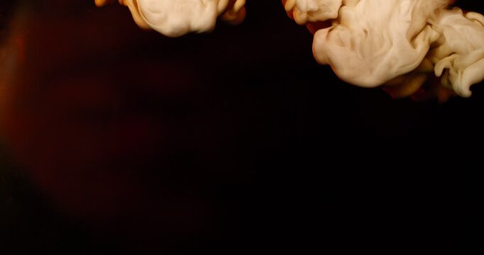 Extreme super slow motion of milk swirling and mixing into coffee, creating smooth creamy clouds and fluid abstract shapes in a dark liquid background.