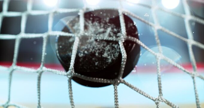 Extreme super slow motion close-up of an ice hockey puck striking the goal net at 1000 fps, with ice particles exploding on impact and a blurred winter stadium and rink in the background.
