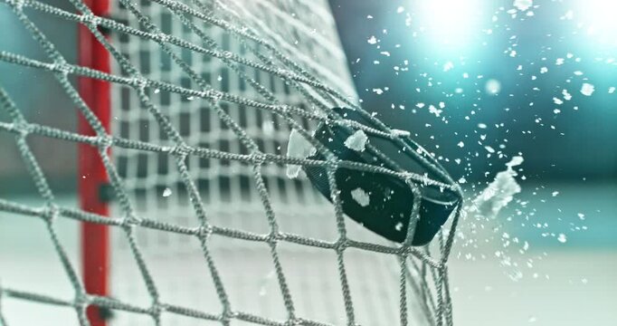 Extreme super slow motion close-up of an ice hockey puck striking the goal net at 1000 fps, with ice particles exploding on impact and a blurred winter stadium and rink in the background.