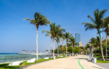A scenic view of the Roshn Waterfront Walkway in Jeddah, Saudi Arabia, featuring palm trees and modern architecture along the Red Sea coast.