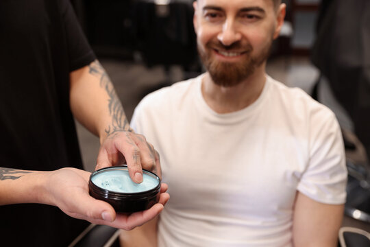 Barber with styling product and his client indoors, closeup