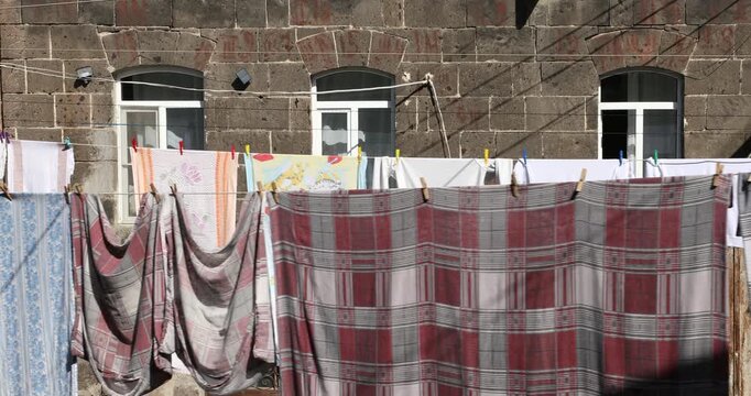 A slow panning shot reveals colorful laundry hanging on a clothesline to dry in the bright sunlight, strung across a courtyard in front of an old stone building.