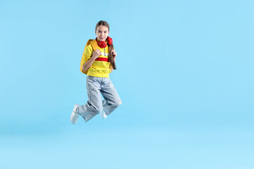 Obraz premium School holidays. Cute schoolgirl with backpack and headphones jumping on light blue background, space for text