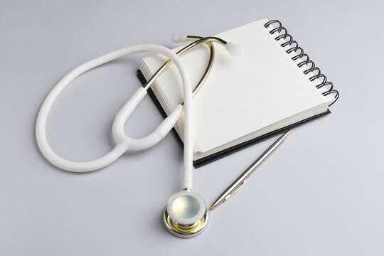 White stethoscope, notepad and pen on grey background