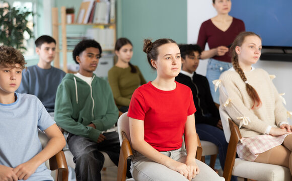 Teenage children sit in the classroom and look at the presentation against the background of the teacher. Boys and girls at school watching a documentary