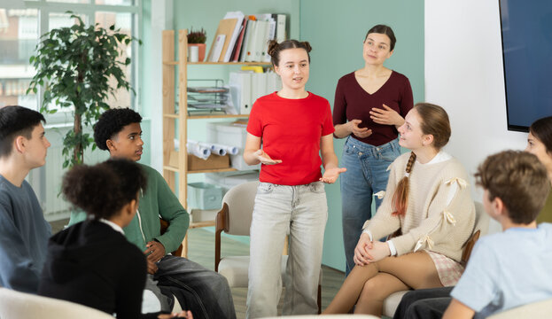 Teen group sit in circle and listen to girl classmate speaking, teacher watching. Acting masters courses, stage speech courses, public speaking courses