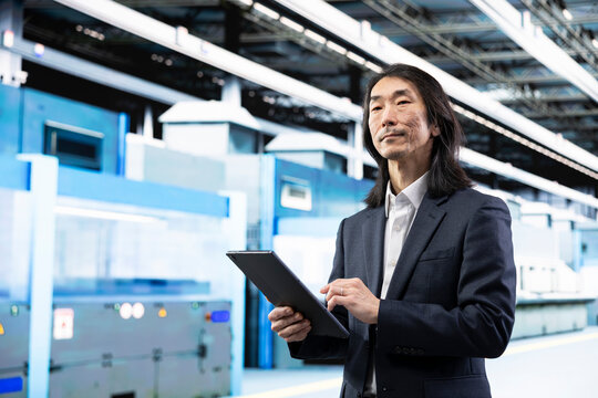 Businessman in industrial PCB production fab planning manufacturing strategy using tablet. Microchip foundry director analyzing automated machinery operational data with device