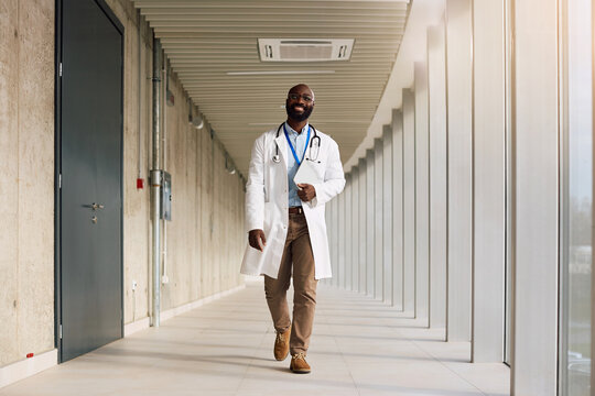 Happy black doctor walking through hallway at medical clinic.