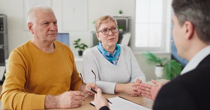 Seniors couple meet advisor and agent for contract. Clients discuss paperwork in a meeting in a bright office, weighing housing and insurance. Clear financial consultation guidance concept here.