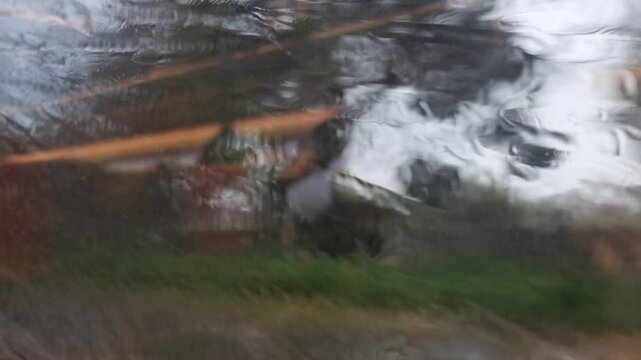 Train travel with rainy view through a train window with blurred countryside and water droplets on glass. Motion-blurred rural scenery seen through a wet window