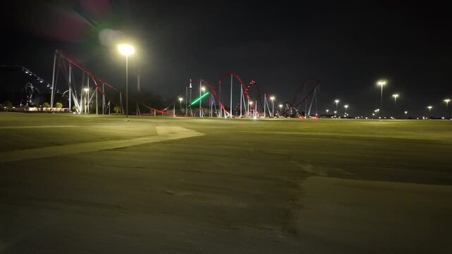 Driving Past a Rollercoaster Theme Park at Night in an Empty Lot