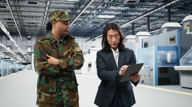 Soldier speaks with microchip production factory senior manager about using microelectronics for national security operation. Army officer and Asian man chat about semiconductor supply chain, camera A