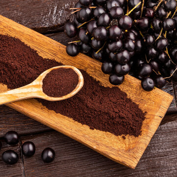 Round, shiny acai berries accompanied by a handcrafted scoop of dehydrated acai powder. - Euterpe oleracea